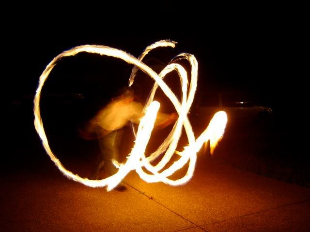 Long exposure of fire poi tracing a wide spiral across a dark road